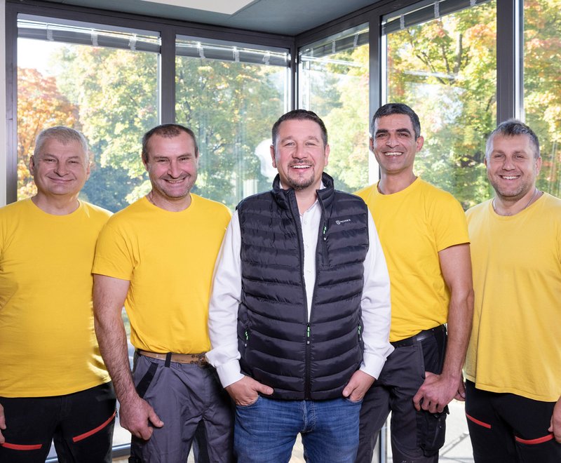 SWG Team Fünf Männer stehen nebeneinander, vier tragen gelbe T-Shirts, einer eine schwarze Weste. Sie lächeln freundlich und blicken in die Kamera.