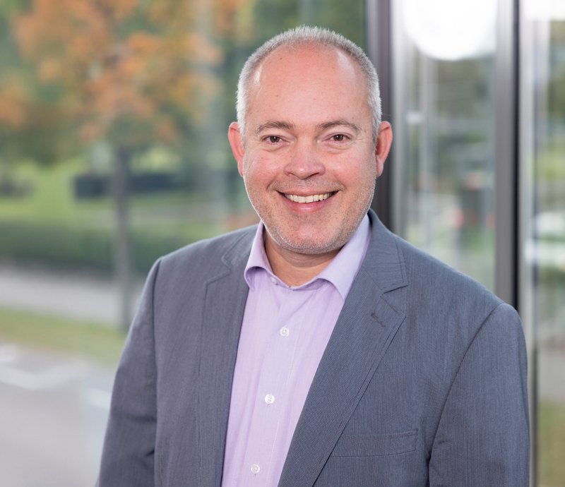 Matthias Buck Leiter Mieterservice Porträt eines lächelnden Mannes mittleren Alters, der einen hellen Hemdkragen unter einem grauen Sakko trägt.