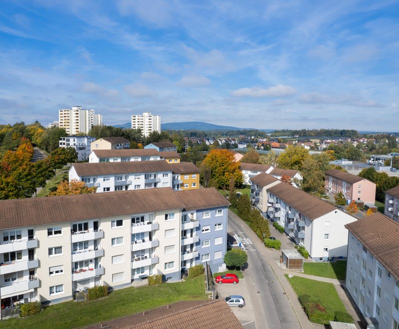 Luftaufnahme einer Wohnsiedlung Luftaufnahme einer Wohnsiedlung mit mehrstöckigen Wohnhäusern, umgeben von Bäumen und grünen Flächen, unter einem blauen Himmel mit vereinzelten Wolken.