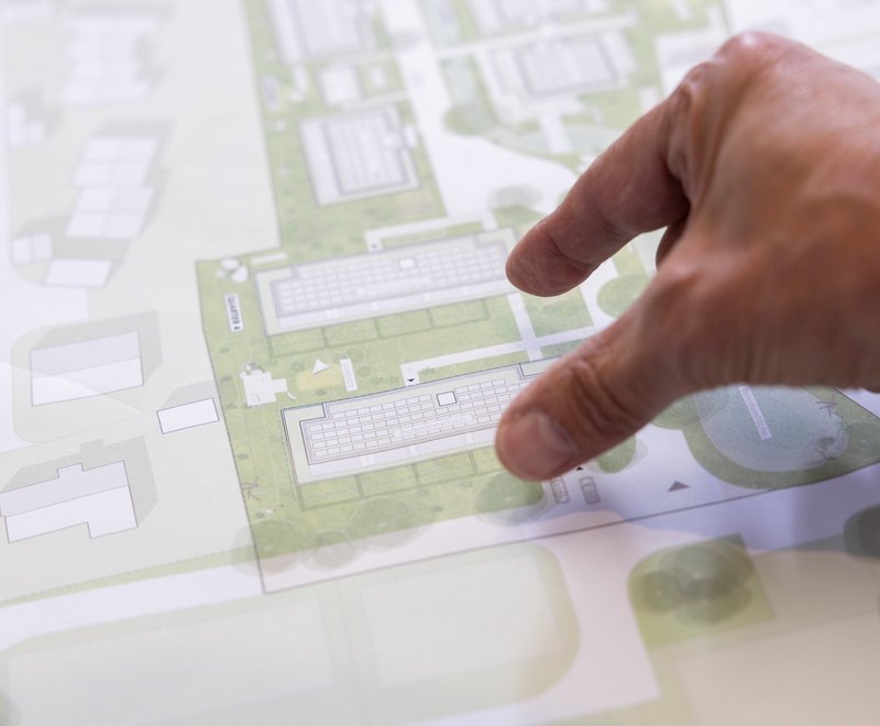 Bauplan der SWG Eine Hand zeigt auf einen detaillierten Stadtplan oder Bauplan mit Gebäuden und grünen Flächen.