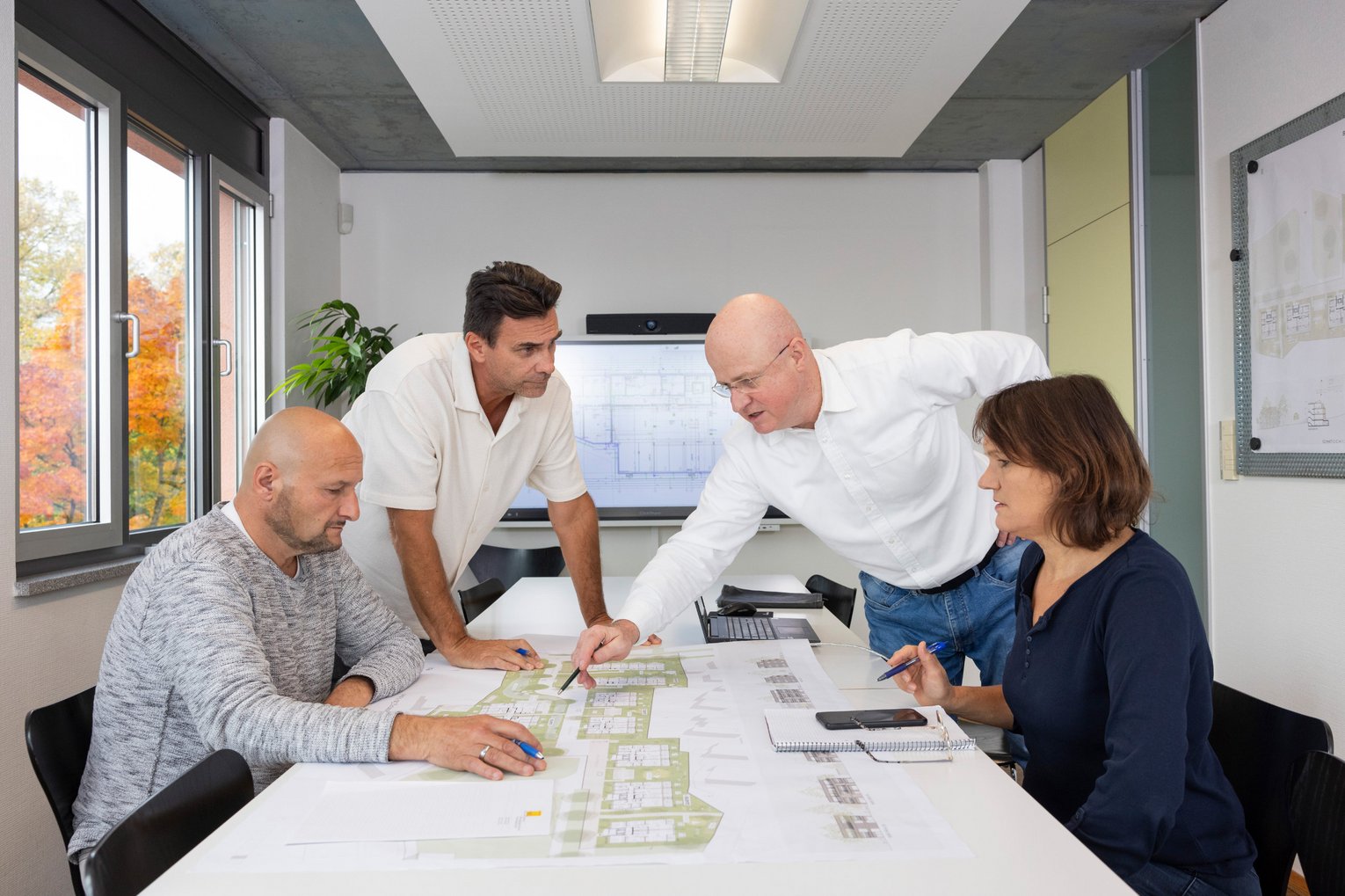Besprechung bei der SWG Friedrichshafen Vier Personen besprechen gemeinsam Baupläne auf einem Tisch in einem modernen Besprechungsraum.