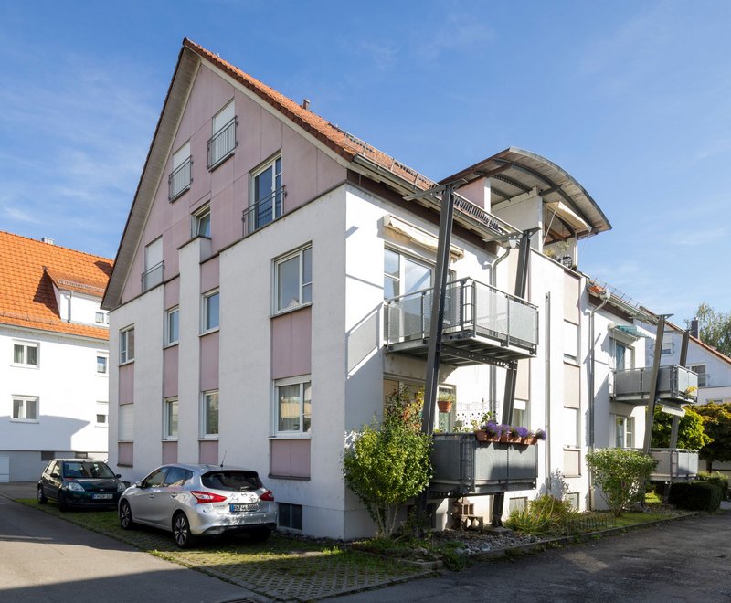 Allmandstraße SWG Mehrstöckiges Wohngebäude mit Balkonen, weißen und rosa Fassaden, roten Dächern und geparkten Autos an der Straße bei sonnigem Wetter.
